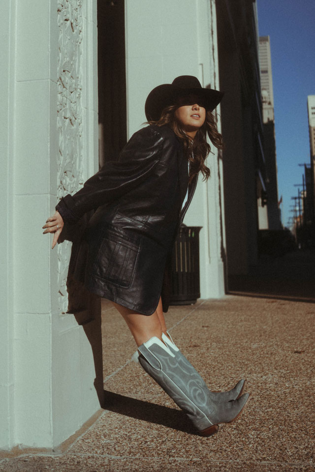 A woman wearing Justin Vintage boots leaning against a wall.